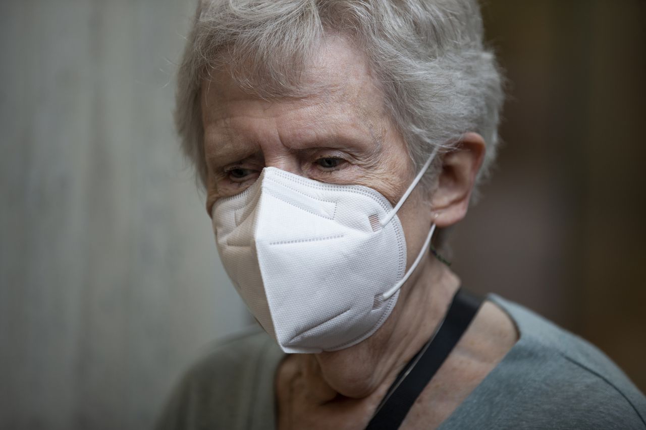 A woman with grey hair wearing a white face mask in medium close up