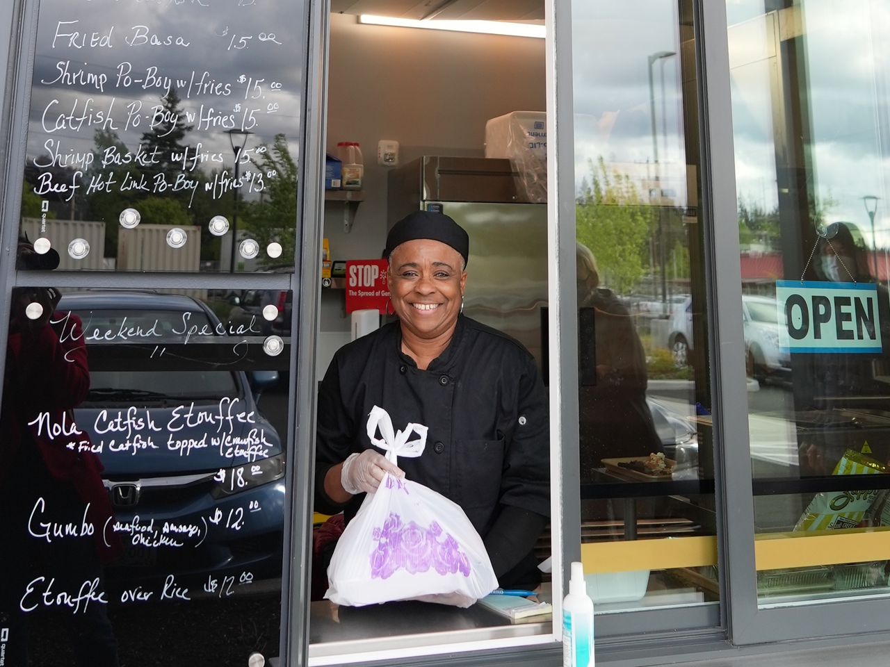 smiling woman hands a container of food from a restaurant ordering window