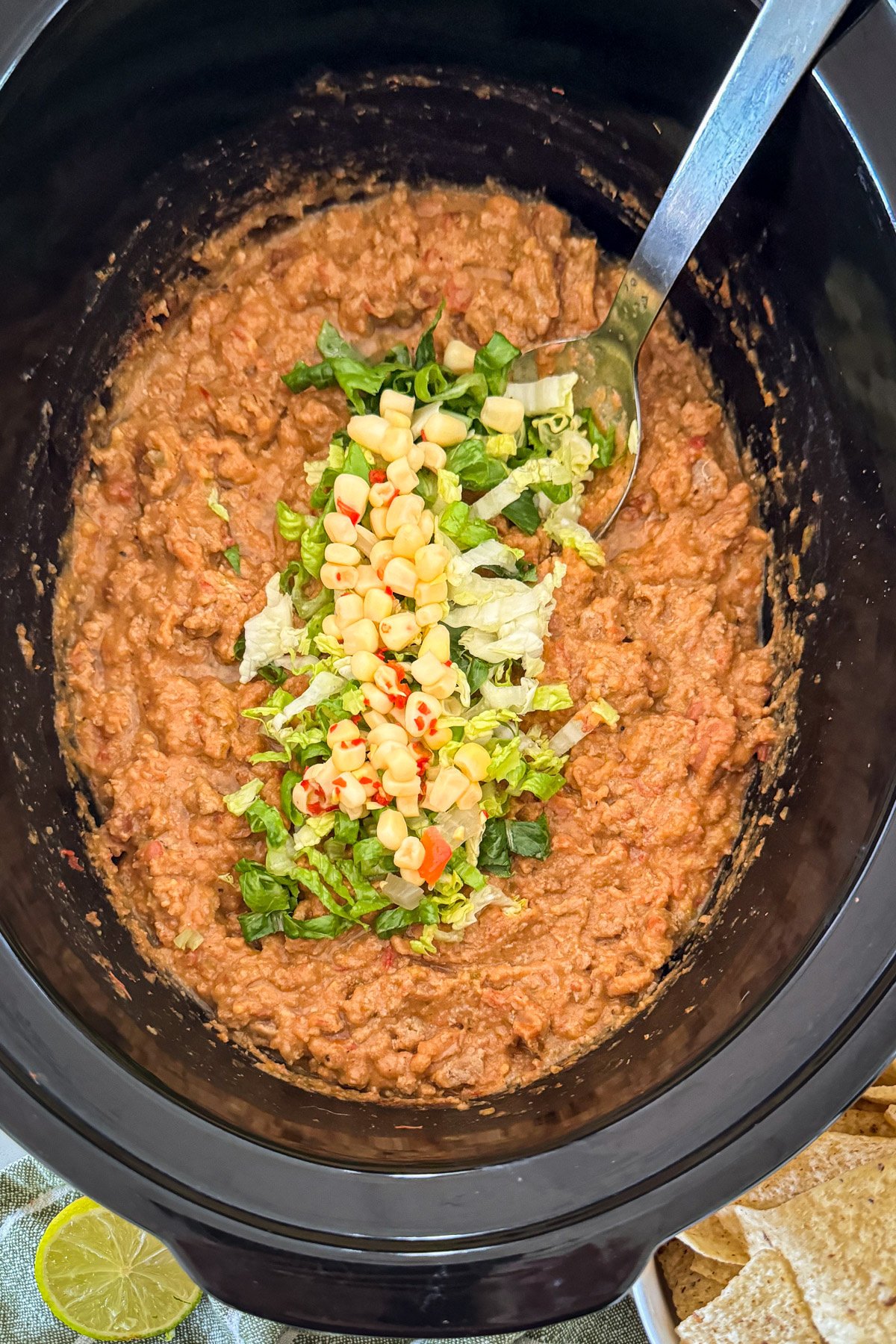 taco dip with toppings in black bowl of a slow cooker from above