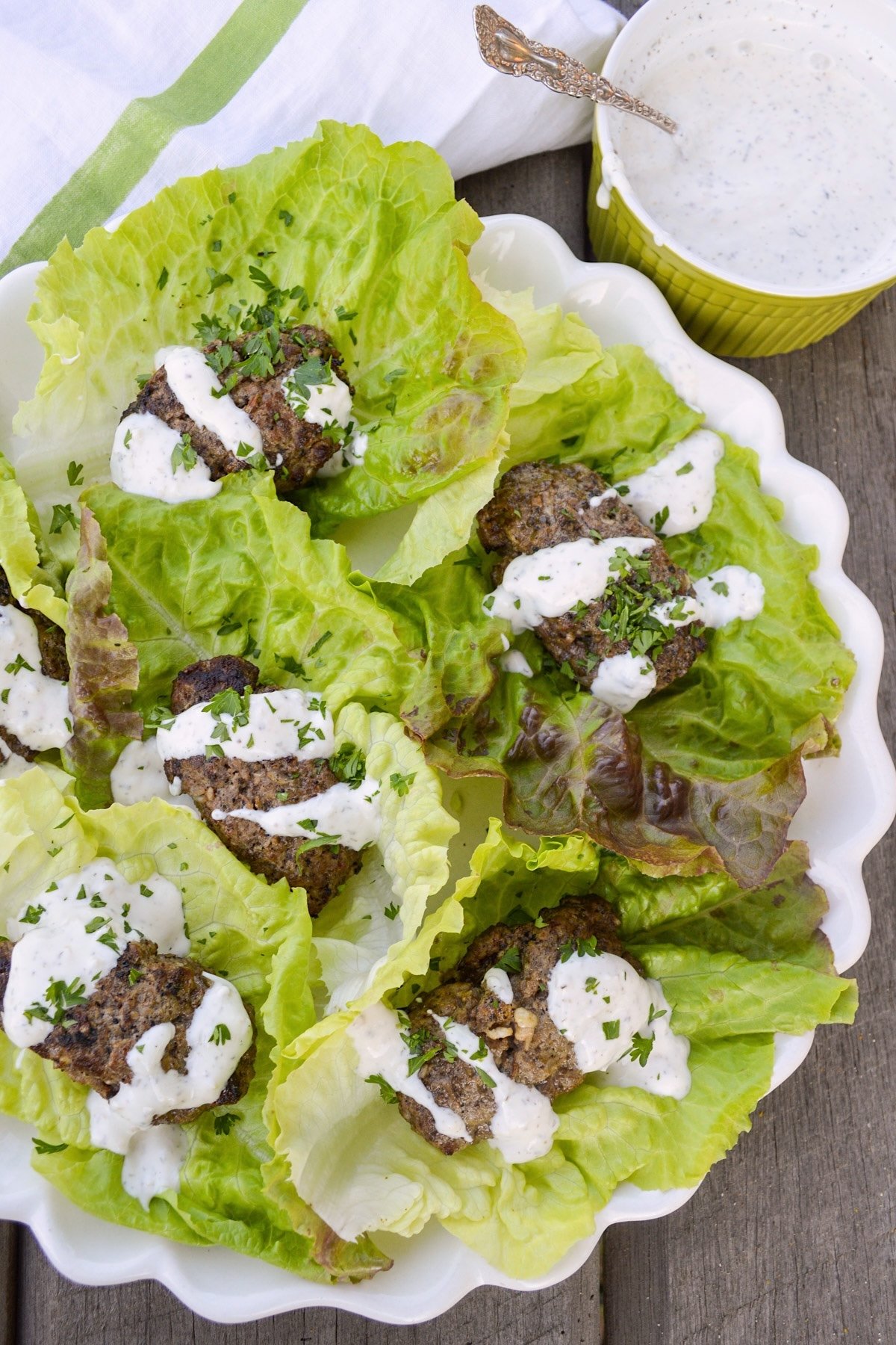 beef patties in lettuce wraps with yogurt sauce on white platter